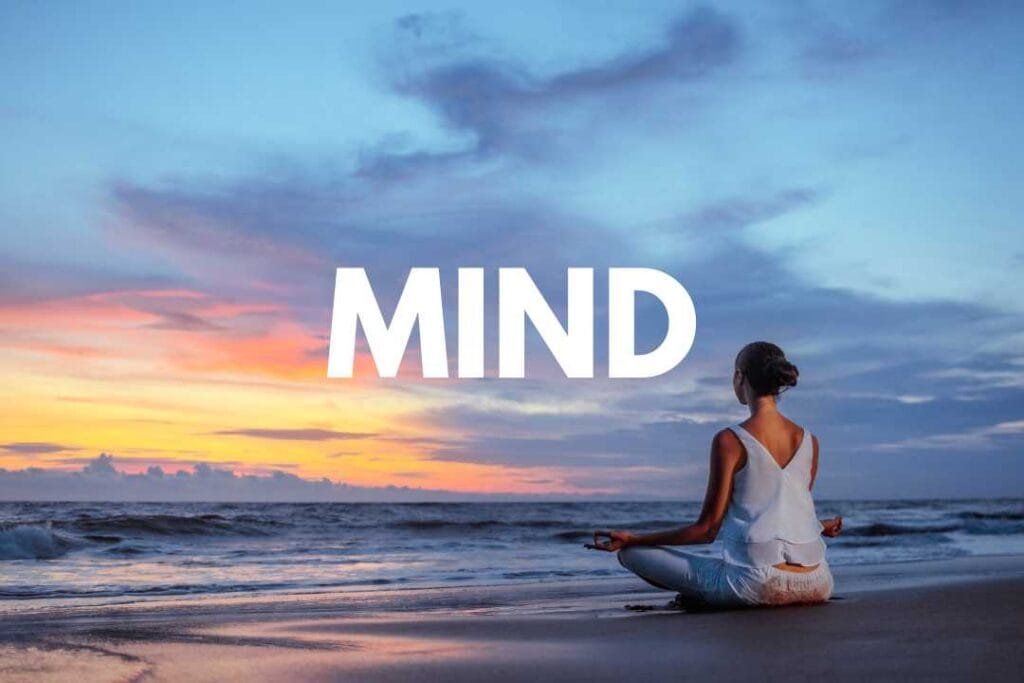 Woman meditating on a beach barefoot at sunset