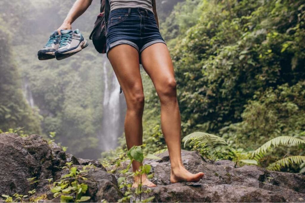 Barefoot hiking, a woman walking by a waterfall barefoot and holding her shoes in her hands