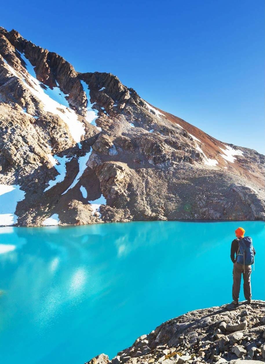 a man with a backpack hiking by a blue lake and glaciers.