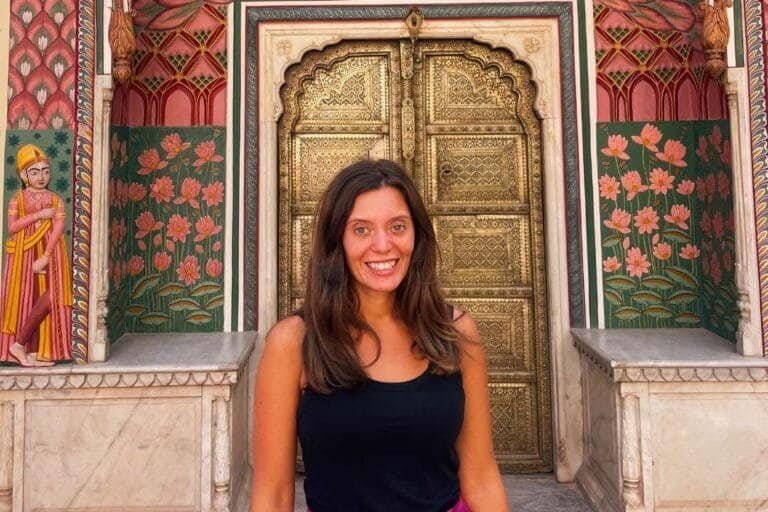 Colorful Indian temple entrance with intricate gold door and traditional floral artwork, featuring a smiling traveler enjoying cultural sightseeing at Barefoot Backpackers.