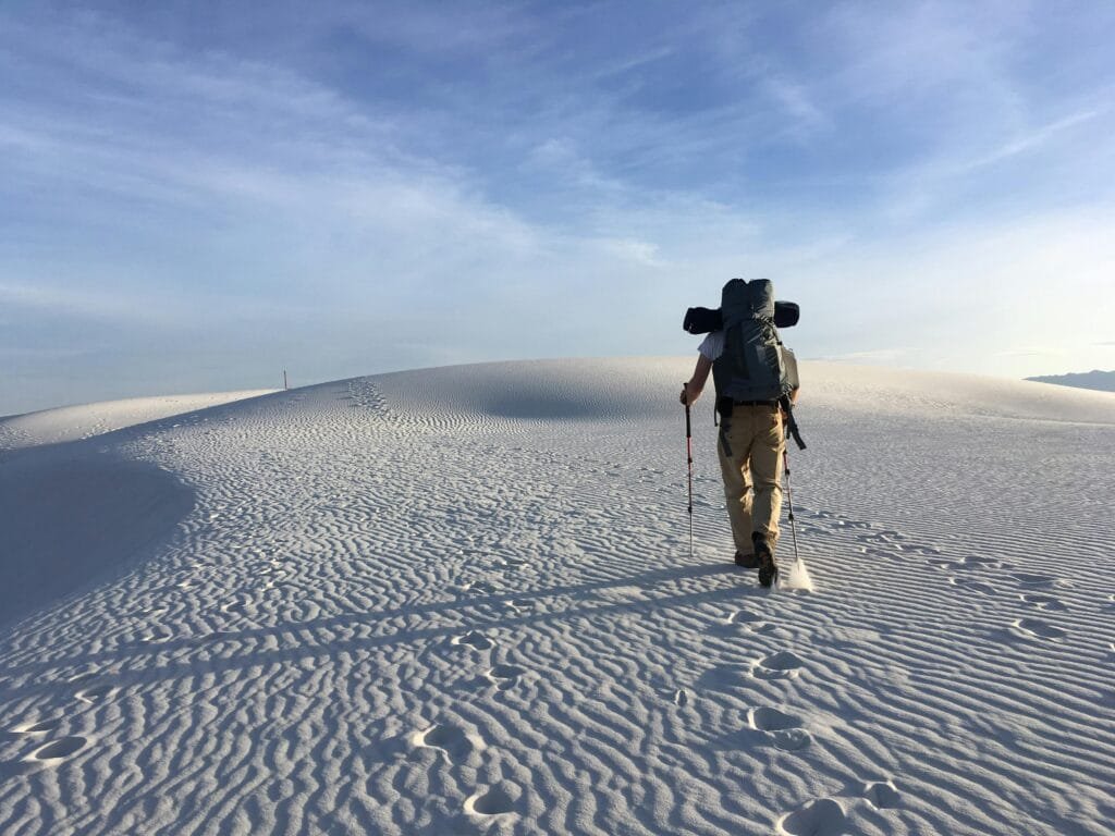 A lone hiker traverses the white sand dunes of White Sands National Park under a clear sky.