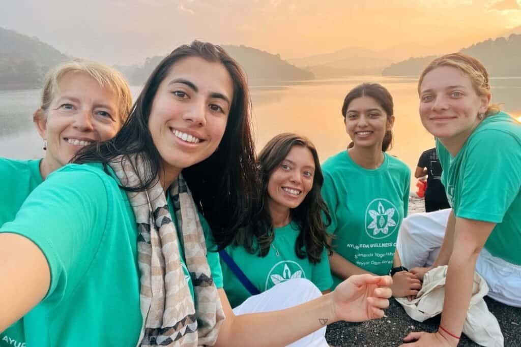 Sivananda Happy women enjoying sunrise by a serene lake during a mindful outdoor wellness retreat.