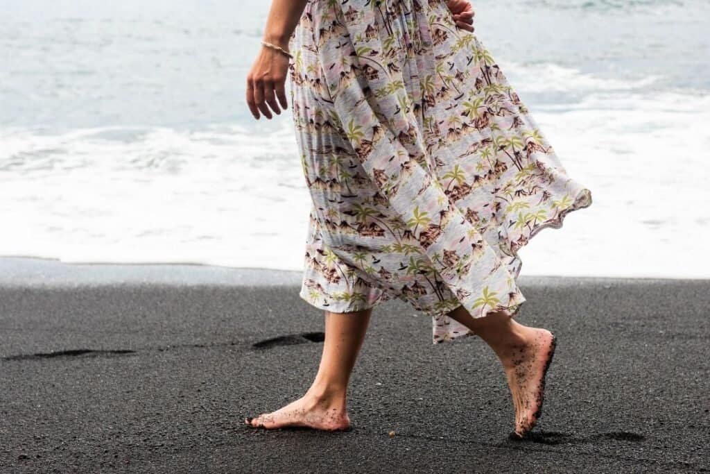 Barefoot woman walking on black sand beach, embracing natural travel experiences and sustainable lifestyle.