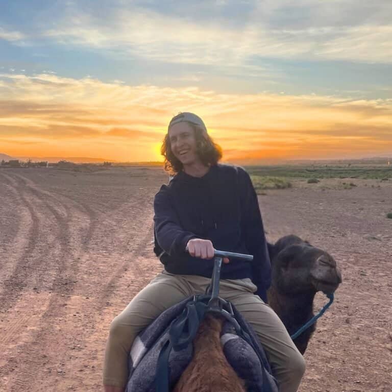 Greg, co-founder of Barefoot Backpackers, riding a camel at sunset
