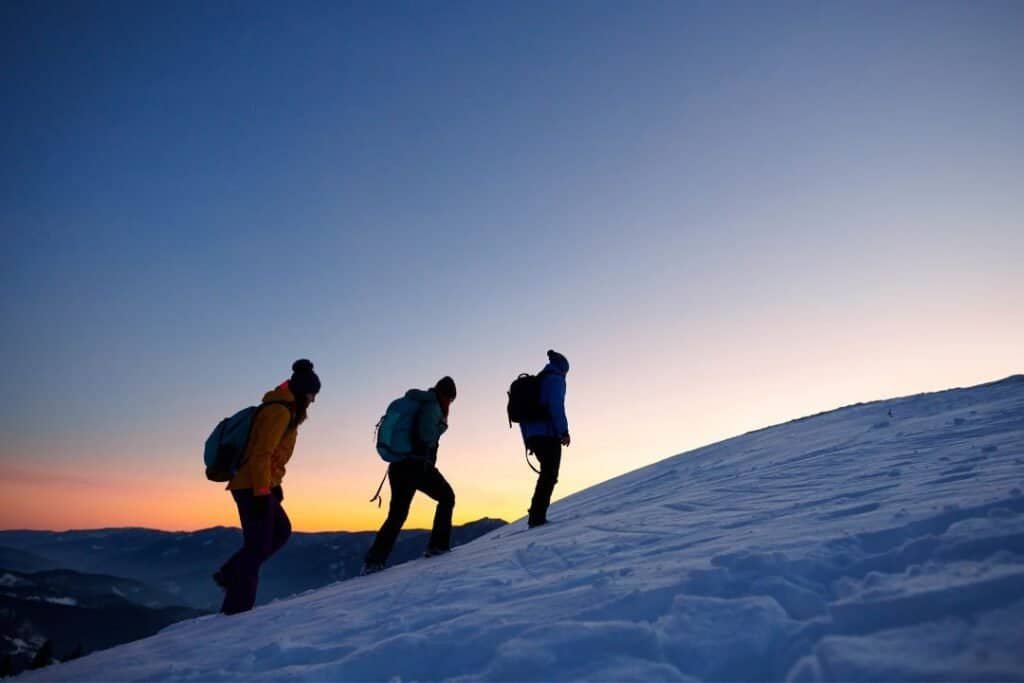 Hikers ascending snowy mountain slopes at sunset, embracing mindful outdoor adventure and sustainable travel practices.