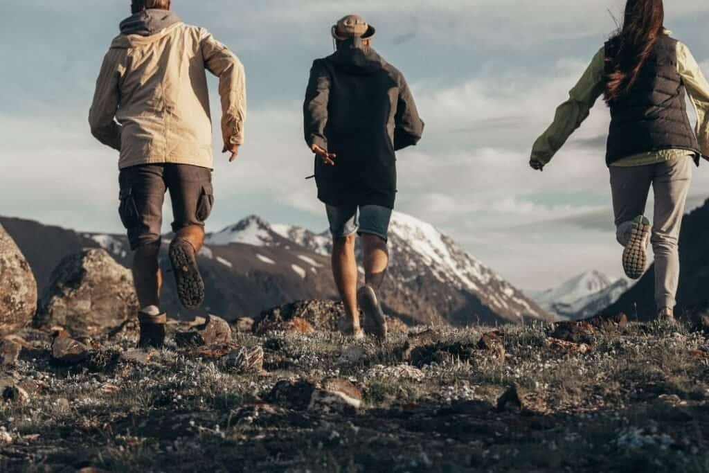 Backpacking friends hiking in mountainous landscape with snow-capped peaks and rocky terrain, exploring nature sustainably and mindfully for adventure lovers.