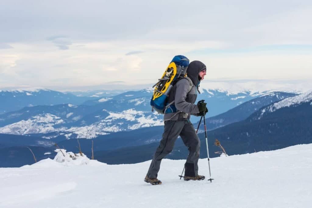 A person trekking in snow-capped mountains with a backpack and trekking poles, embracing sustainable outdoor adventure and mindful exploration.