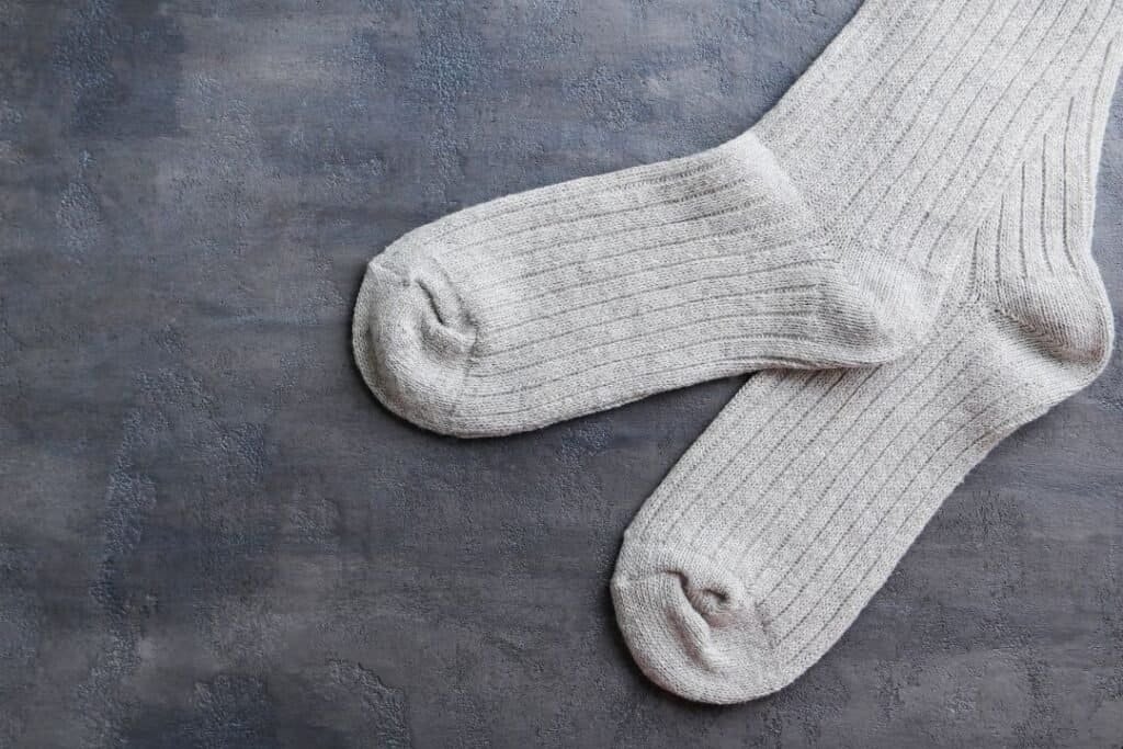 Comfy beige knitted socks on a textured gray surface, highlighting sustainable and cozy footwear options for mindful travelers.