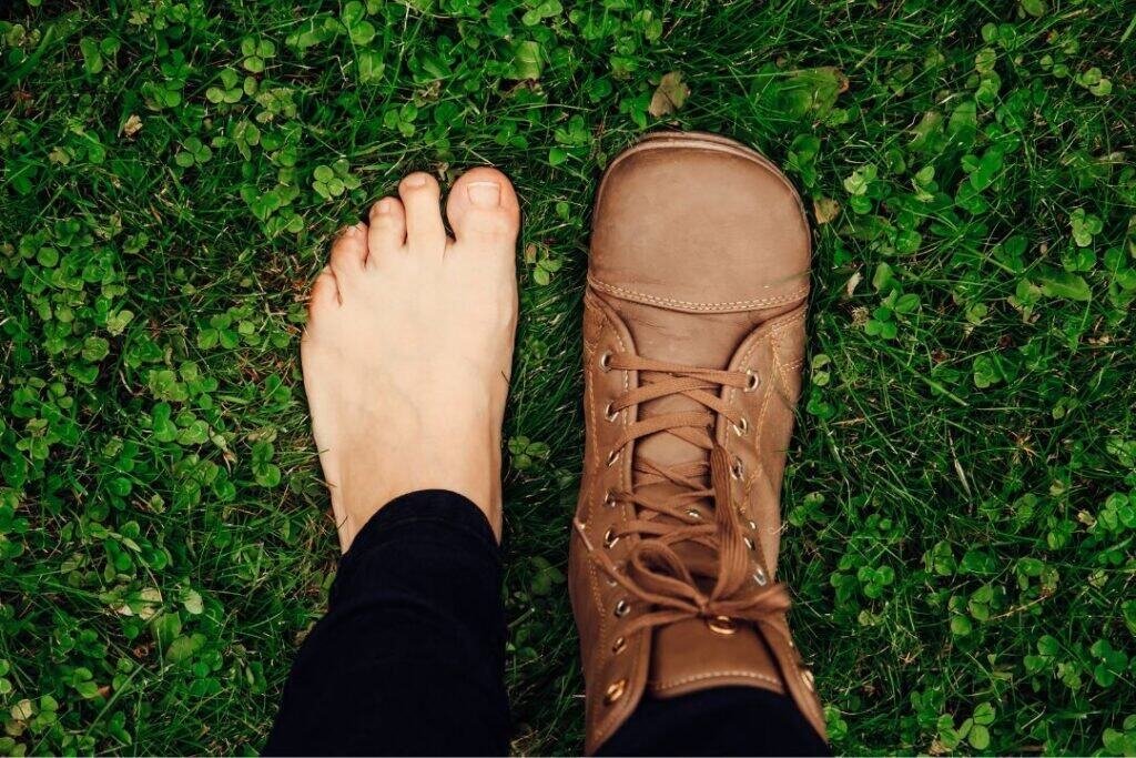 Barefoot and booted feet on lush green grass, symbolizing mindful travel and grounding with sustainable exploration.