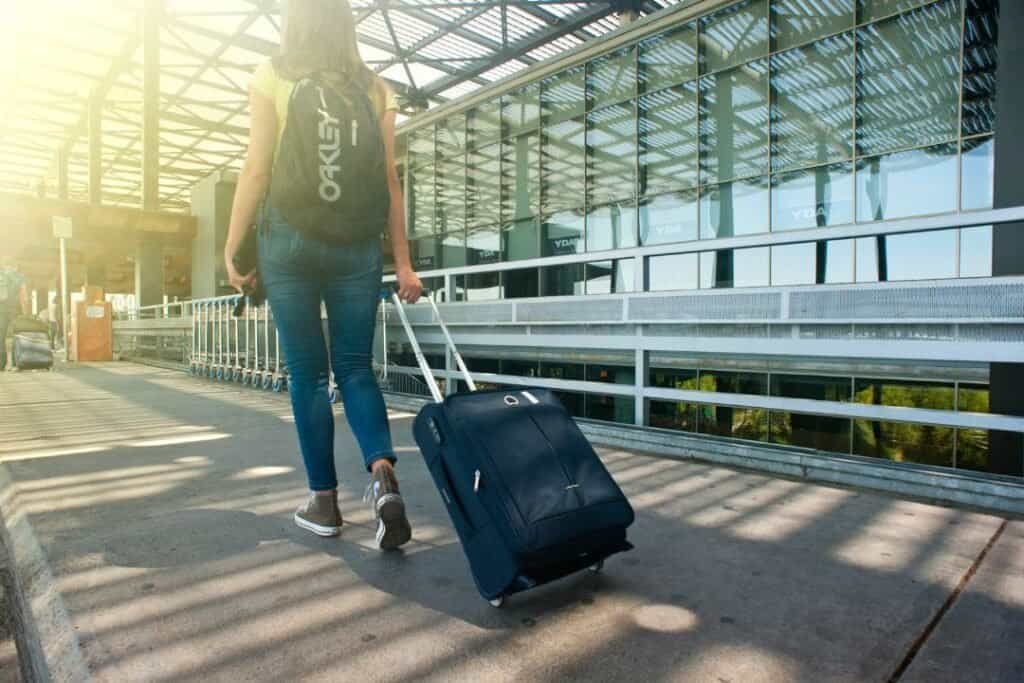 Traveling woman with rolling suitcase outside modern airport terminal for sustainable adventures.