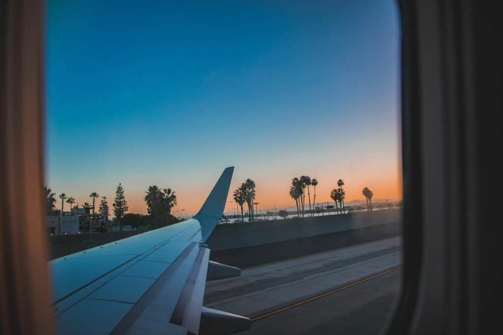 Scenic view from an airplane window of wing and palm trees during sunset.