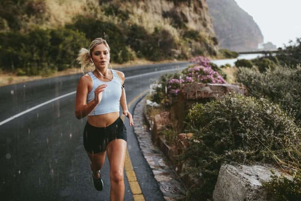 Running woman on scenic mountain road during rain, embracing mindful outdoor activity for holistic travel.
