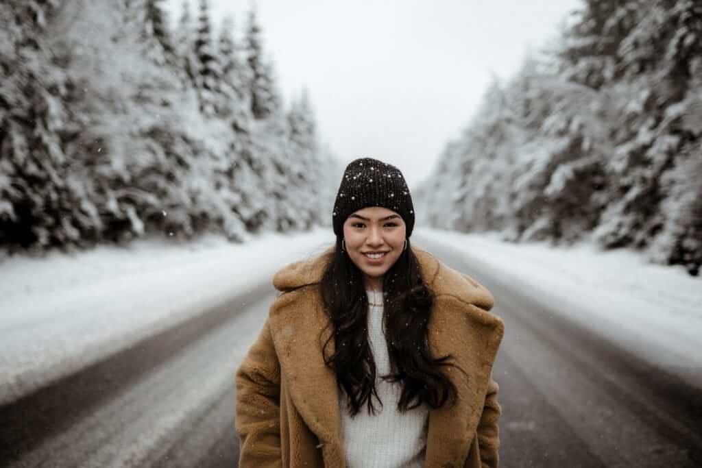 Young woman enjoying a winter hike through a snowy forest landscape with her 100% wool beanie.