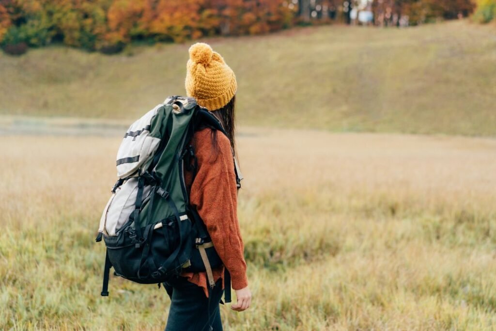 Wanderer with a 50l backpacks for woman exploring a peaceful autumn landscape in a grassy field.