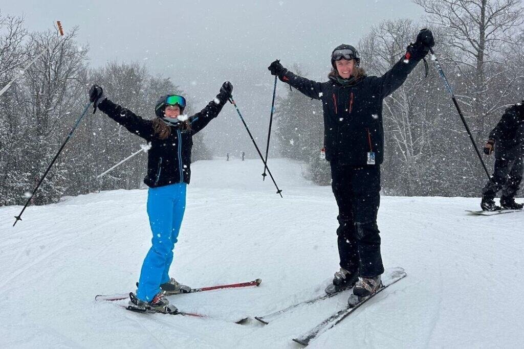 Enjoying winter outdoor adventure: skiers in snow-covered forest with falling snow, embracing sustainable, mindful travel and outdoor exploration.
