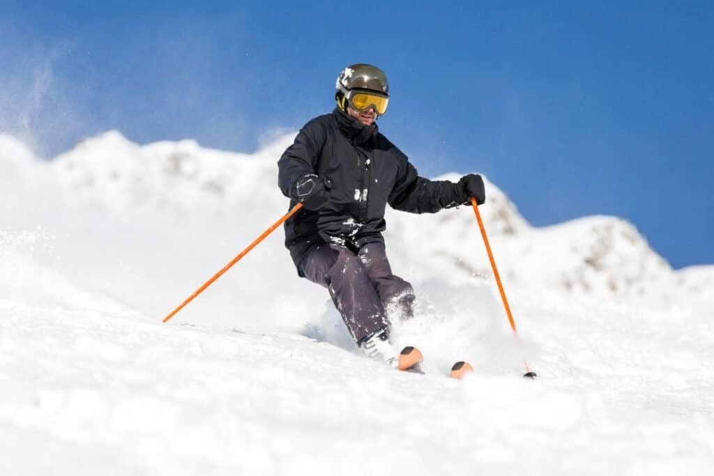 skiing on snowy mountain slope wearing protective gear and goggles under clear blue sky.