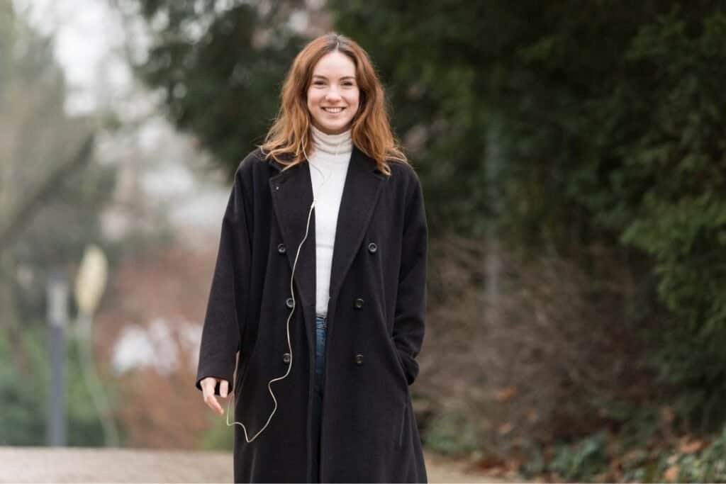 Serene woman walking outdoors in a cozy black coat and listening to music in nature, embodying mindful travel and grounded exploration for holistic adventurers.