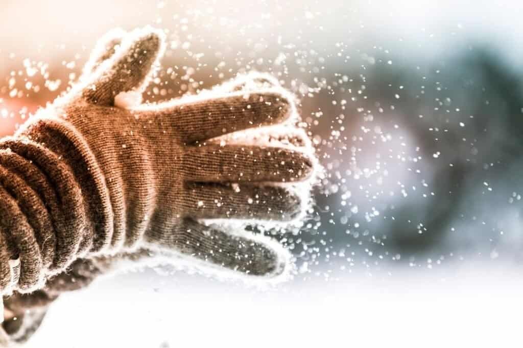 Close-up of 100% Merino Wool Gloves throwing snow, capturing the essence of winter travel and outdoor exploration in cold climates.