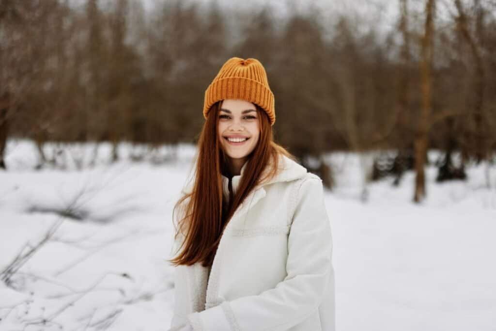 A young woman enjoys a snowy landscape, dressed warmly in a 100% cotton beanie and cozy coat, capturing the peaceful essence of mindful winter travel.