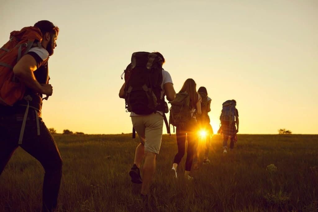 group of backpackers 50l Hiking group at sunset with 50l backpack in a grassy field, embracing mindful travel and connection with nature.