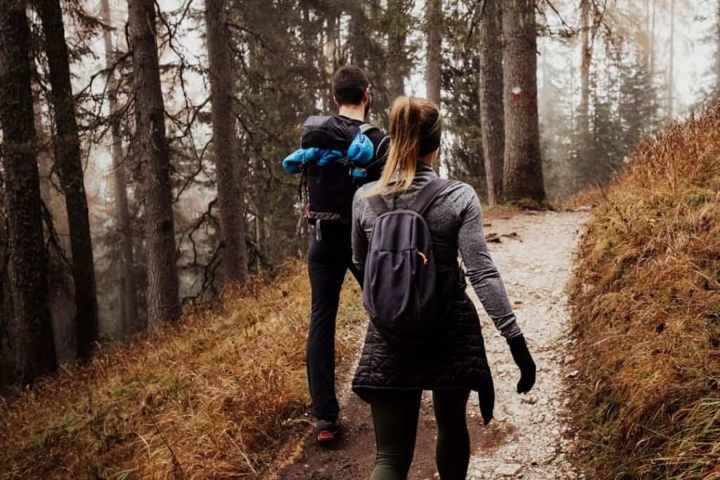 Hiking through a misty forest trail with a man and woman carrying backpacks, surrounded by tall trees and autumn foliage.