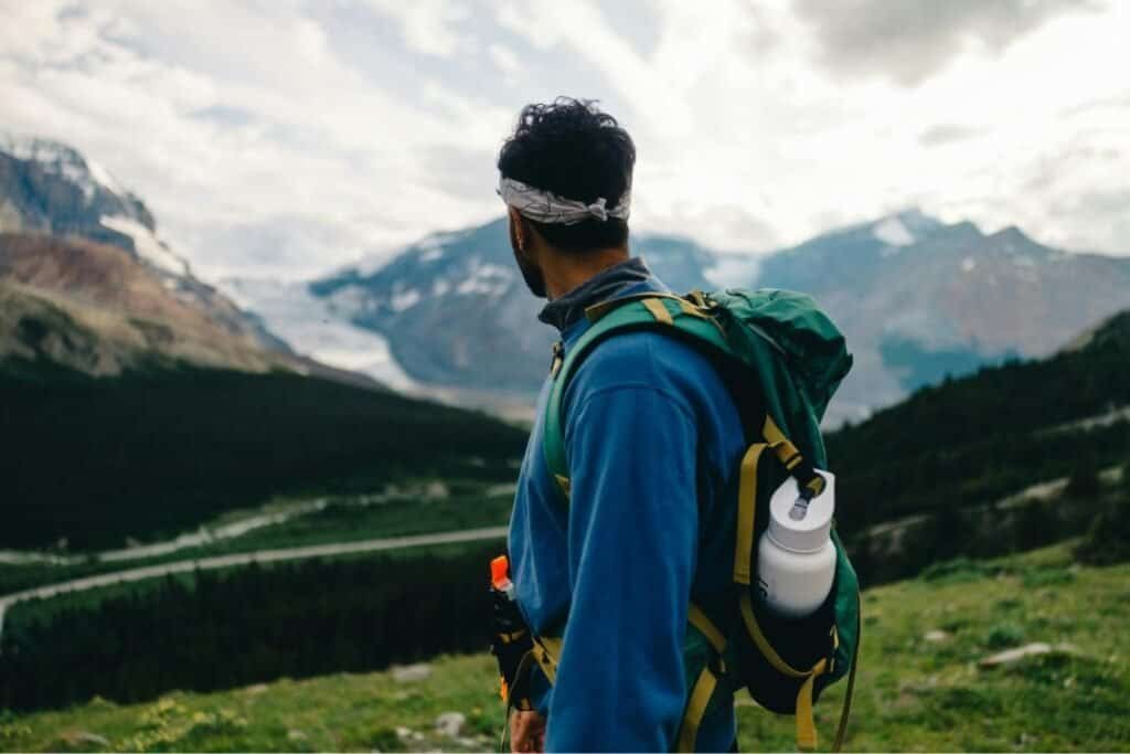 A hiker with a backpack gazes at stunning mountain scenery, embodying mindful, sustainable travel in pristine wilderness.