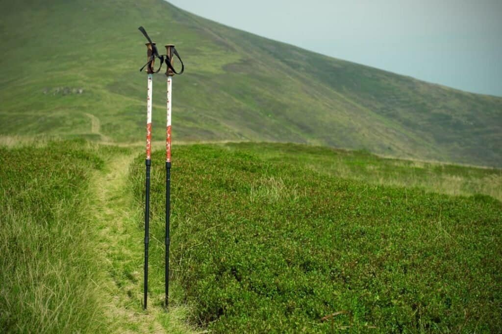 Sliding hiking poles in lush green landscape with rolling hills in the background, inspiring mindful outdoor exploration.