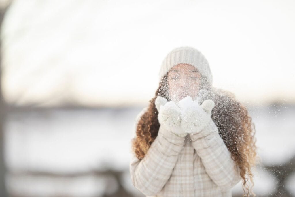 A woman enjoying snowy winter outdoors, dressed warmly with gloves and a beanie, capturing the serene beauty of a snow-covered landscape.