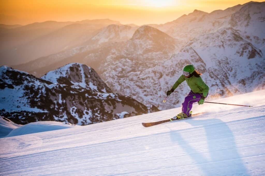 skiing (2) Fresh powder snowboarder skiing down a mountain at sunset, surrounded by snow-covered peaks. Sustainable winter adventure in nature's beauty.