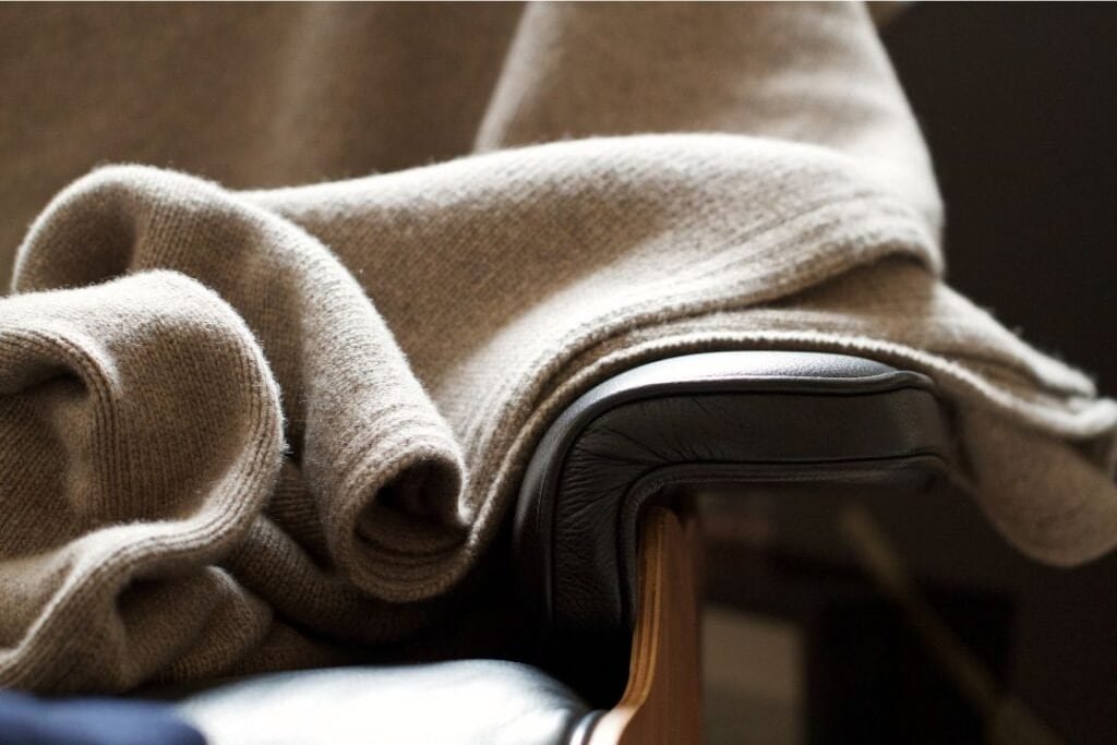 100% Cashmere Blankets draped over a modern wooden and leather chair, creating a cozy and earthy aesthetic perfect for mindful, sustainable living.
