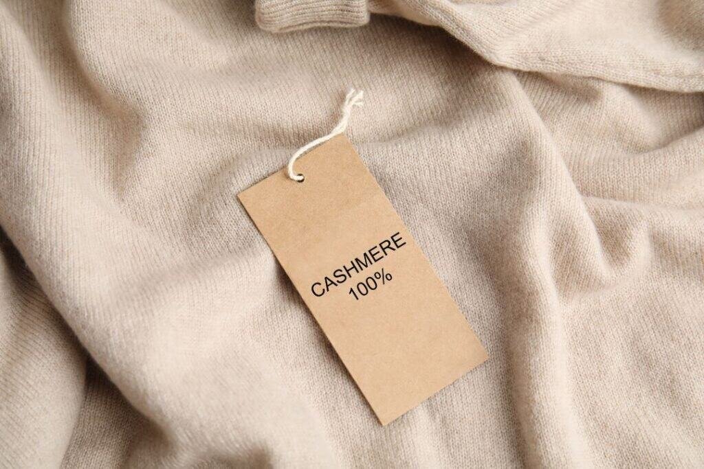 Soft beige 100% Cashmere Sweaters with a twine-tied tag reading "CASHMERE 100%", showcasing luxurious sustainable material.