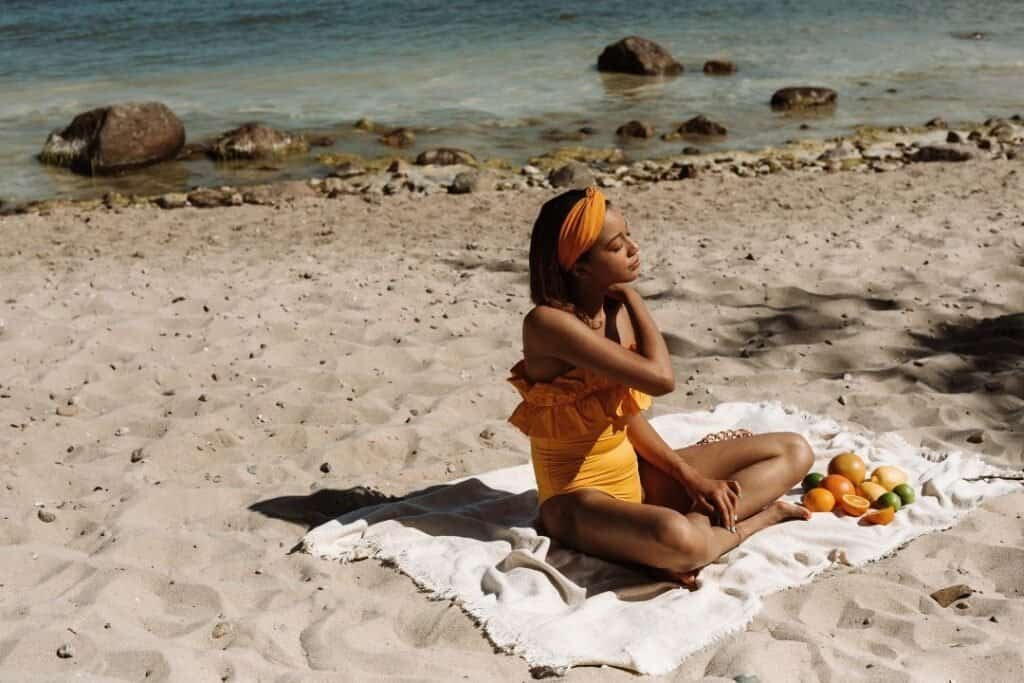 Calm woman practicing mindfulness on a sandy beach with a 100 Cotton throw blanket during sunset, surrounded by nature and the ocean.