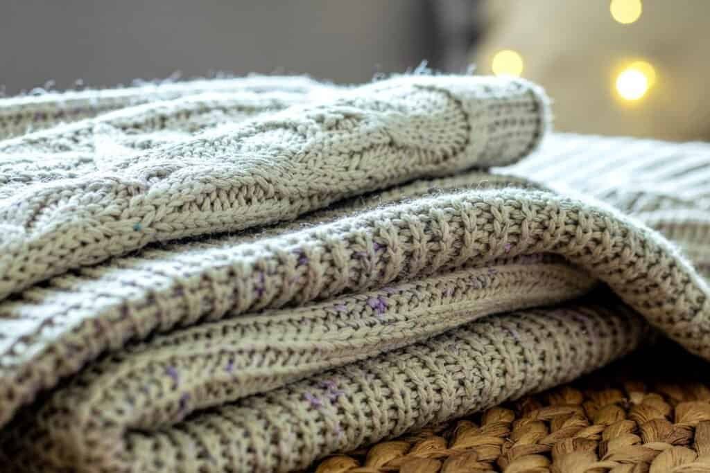 Soft woven 100% sheep wool blankets stacked on a natural woven mat, creating a cozy, sustainable, and eco-friendly ambiance for mindful relaxation.