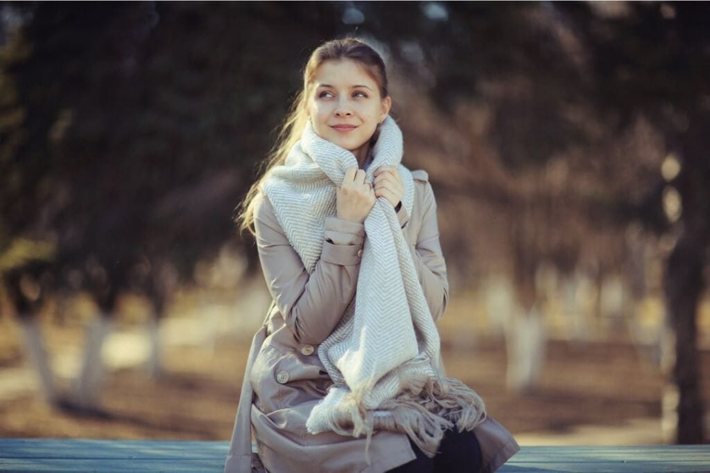 Young woman in a 100% Lambswool Scarf, sitting outdoors in a serene park setting during autumn.