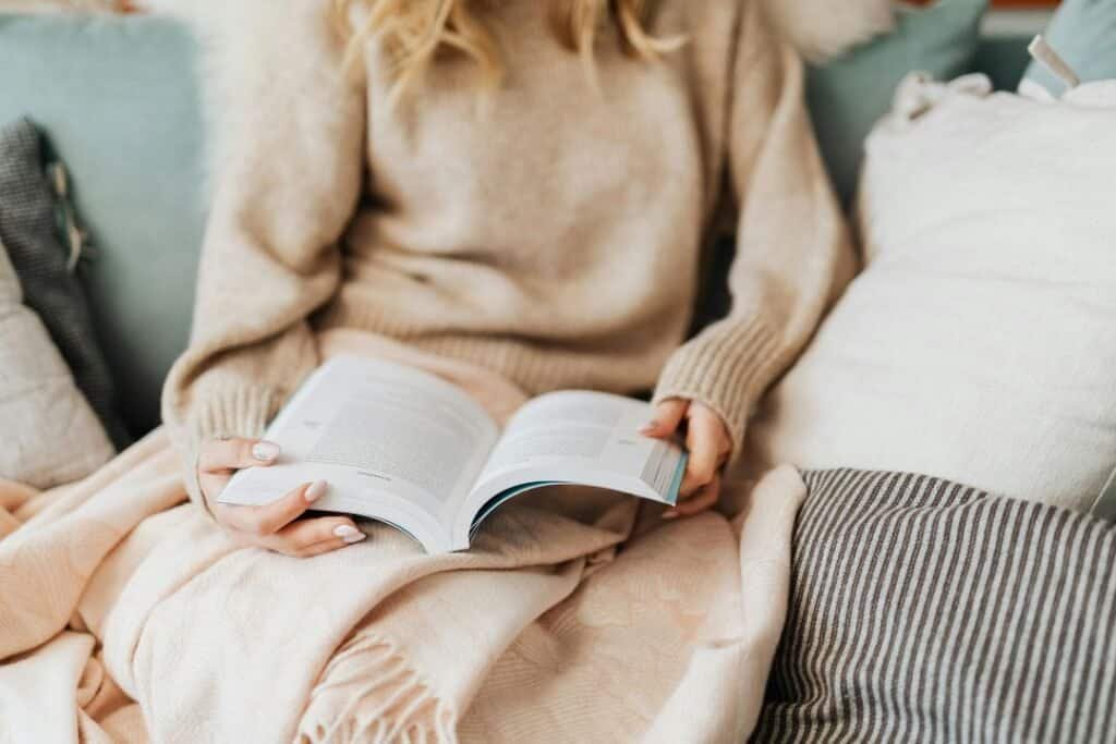 Cozy person reading a book on a couch surrounded with 100% Wool Blankets, exemplifying mindful relaxation and grounding in sustainable travel moments.
