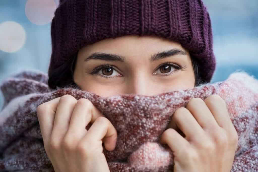 Cozy woman bundled up in a wool scarf and knit hat, enjoying warm winter weather with a mindful, slow approach to travel and lifestyle.