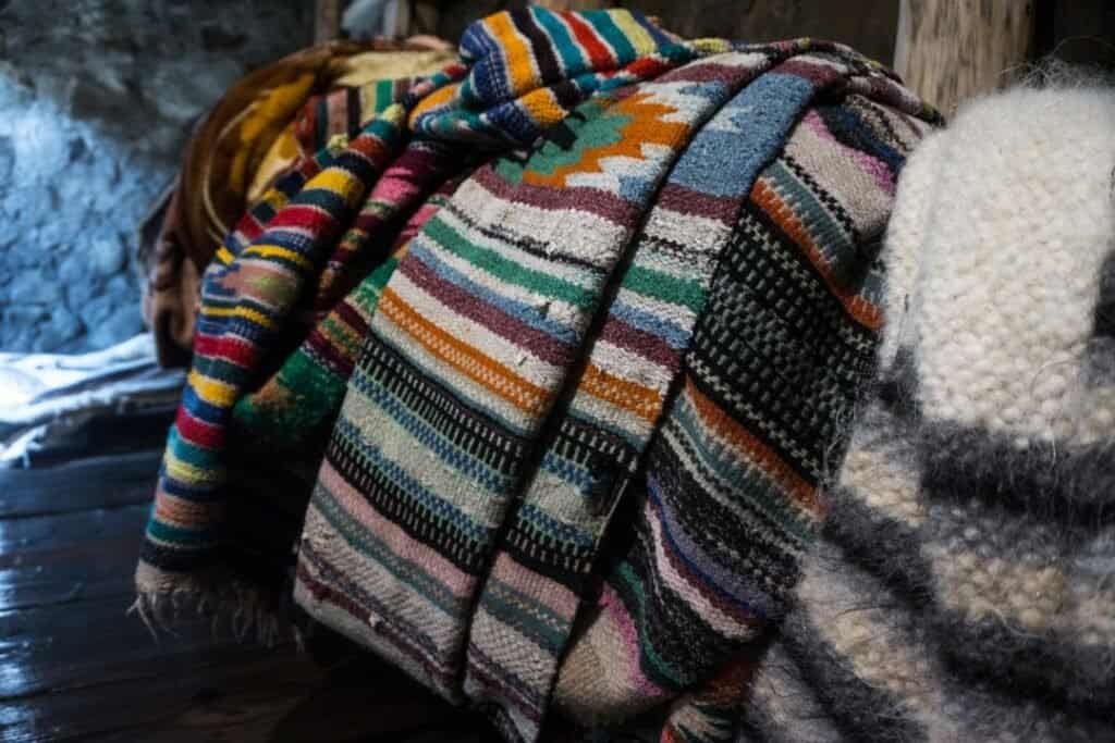 Colorful woven Alpaca Wool Blankets stacked on a rustic wooden surface in an eco-friendly, cozy shelter. Sustainable travel inspires grounded, mindful exploration.