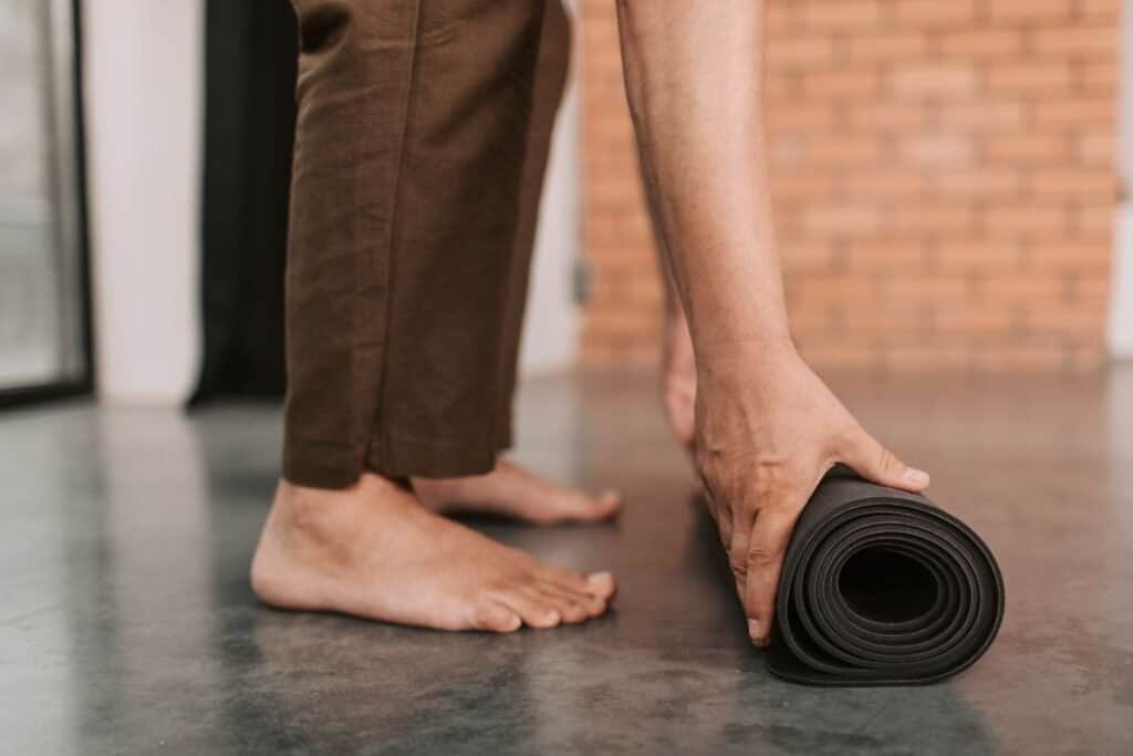 Comfortable person unrolling a travel yoga mat on a wooden floor, emphasizing mindfulness and sustainable lifestyle practices.