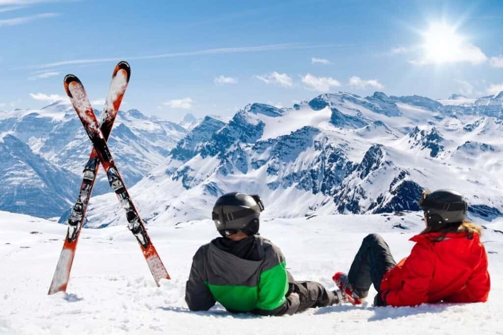 Peaceful snow-capped mountain view with two skiers resting, bright sun, and clear blue sky, inspiring mindful winter adventure.