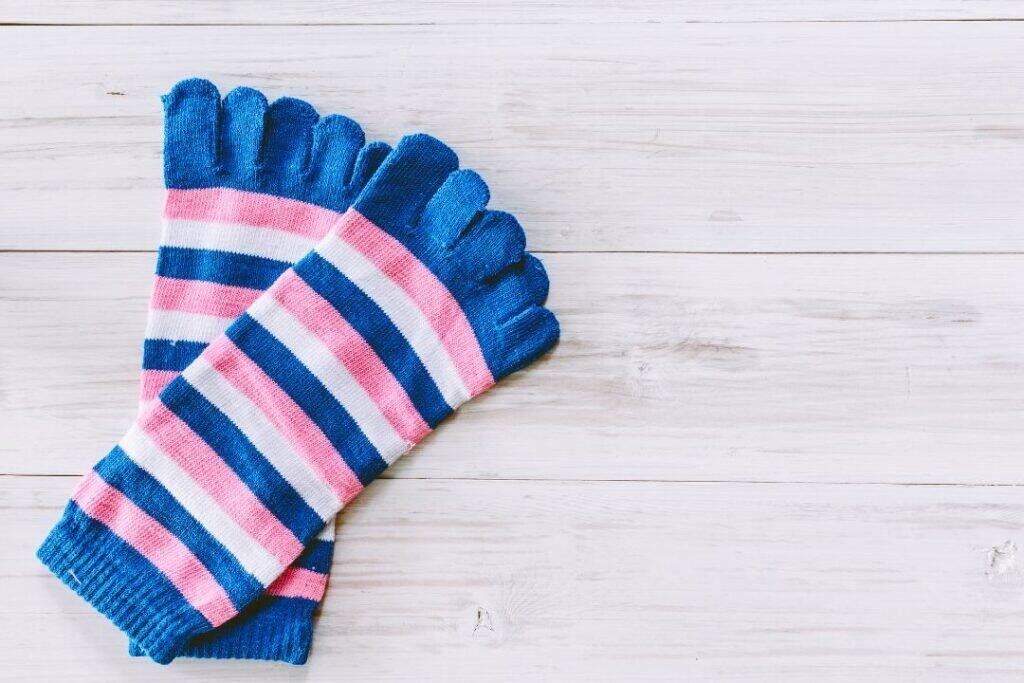 Colorful striped knit Cotton Toe Socks on white wooden background, cozy accessory for eco-friendly travel and outdoor adventures.
