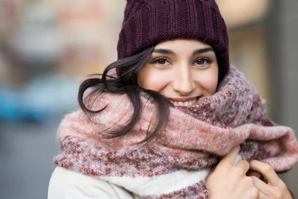 Soft 100% pure cashmere scarf and cashmere beanie on a smiling woman in cold weather, embracing sustainable winter fashion for mindful travel.