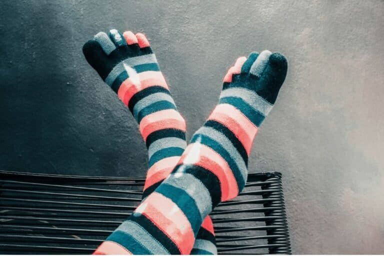 Legs crossed in colorful striped merino wool toe socks on a black metal bench.