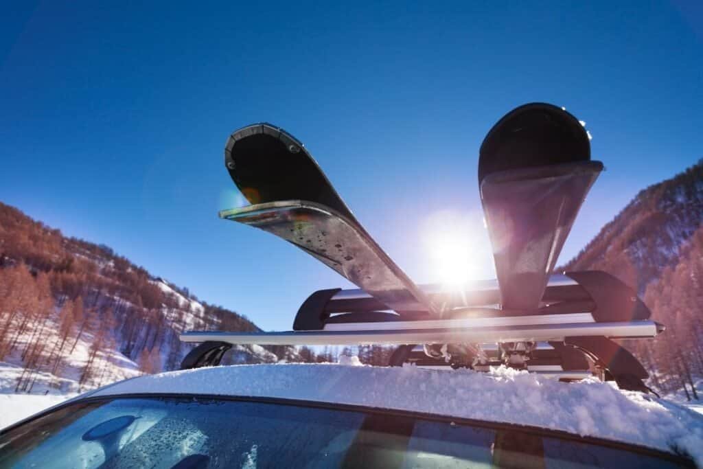 Ski equipment with skis on roof rack in snowy mountain landscape under clear blue sky during winter.