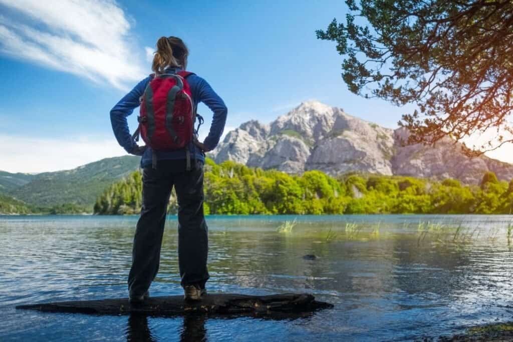 Climber standing on a rock in a serene lake with mountains and a clear blue sky in the background.