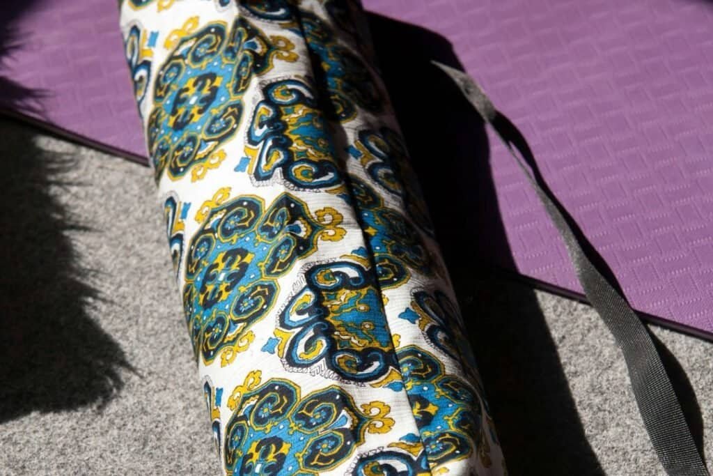 Colorful, patterned yoga mat and bag on outdoor pavement, promoting mindful outdoor workouts and sustainable travel practices for a holistic lifestyle.