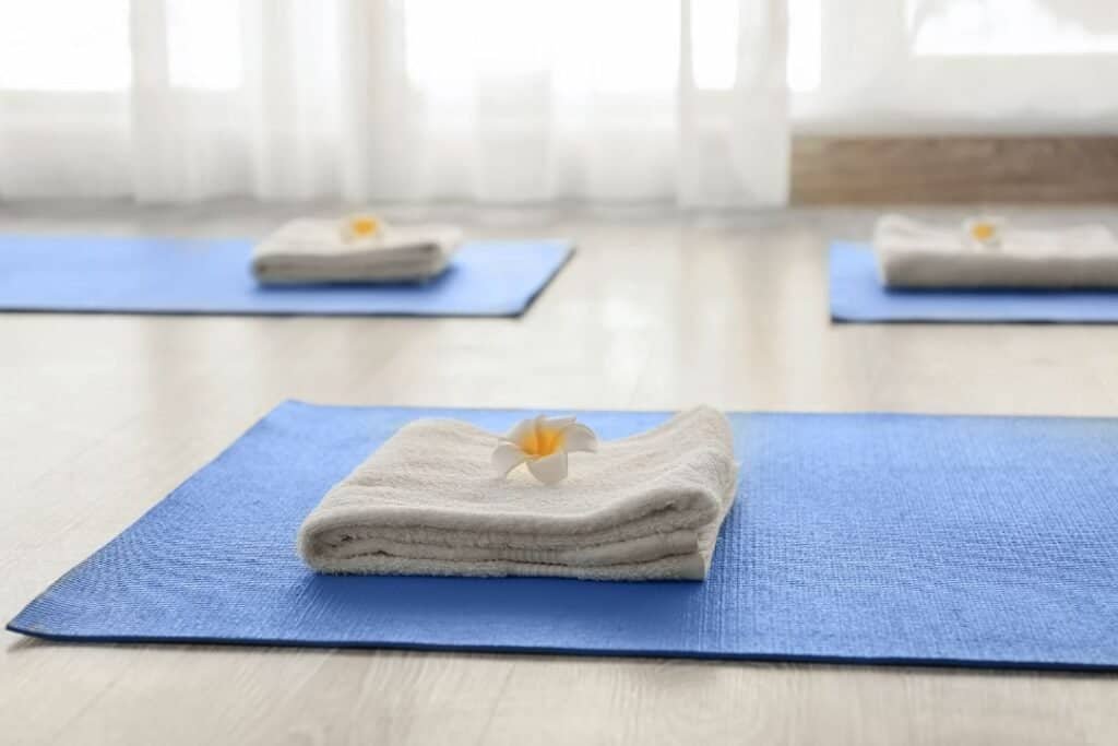 Yoga Mat Towels. Silk white towel with flower on blue yoga mat in bright studio with soft natural light for mindful wellness.