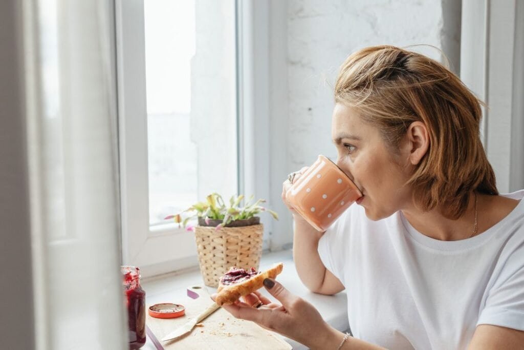 Relaxed woman enjoying breakfast with coffee and toast in cozy kitchen environment.