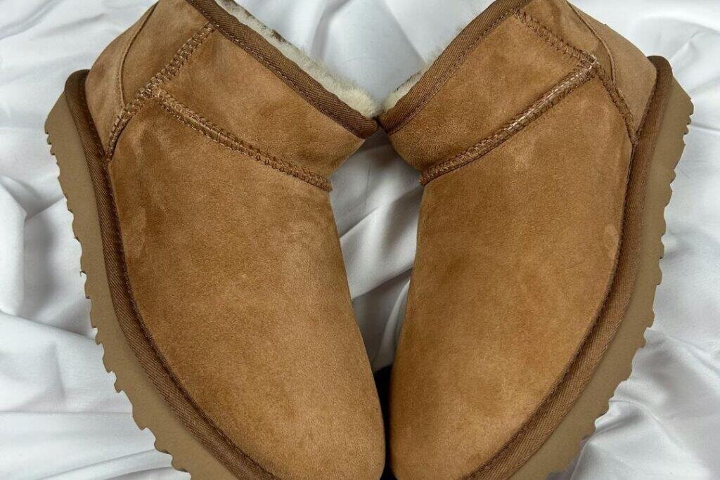 Cozy tan sheepskin-lined winter boots on soft white fabric, perfect for grounding and sustainable travel in cold climates.