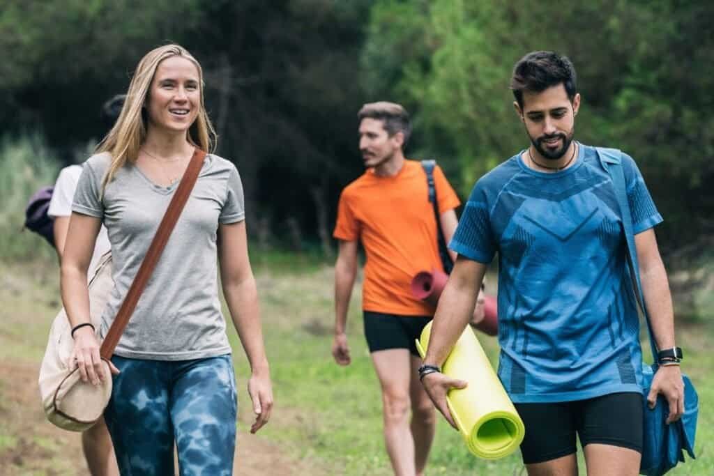 People hiking on a forest trail with a yoga mat and bag enjoying outdoor adventure and mindful exploration in nature.