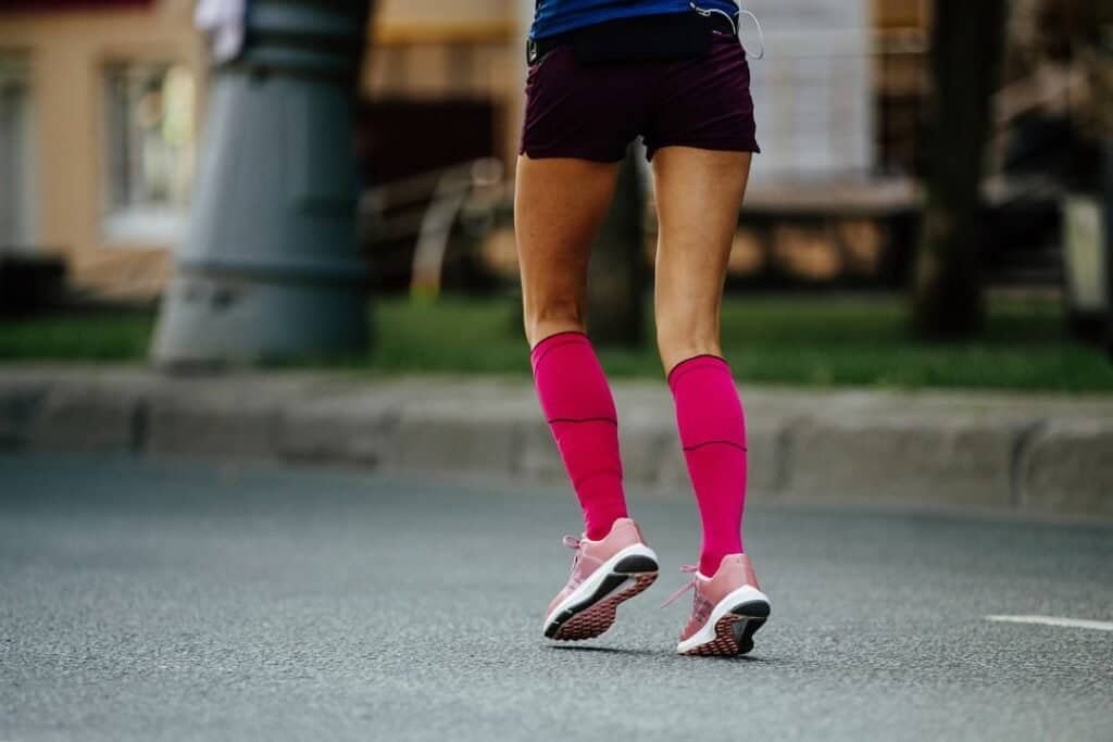 Bright pink compression socks for women paired with running shoes during outdoor exercise.
